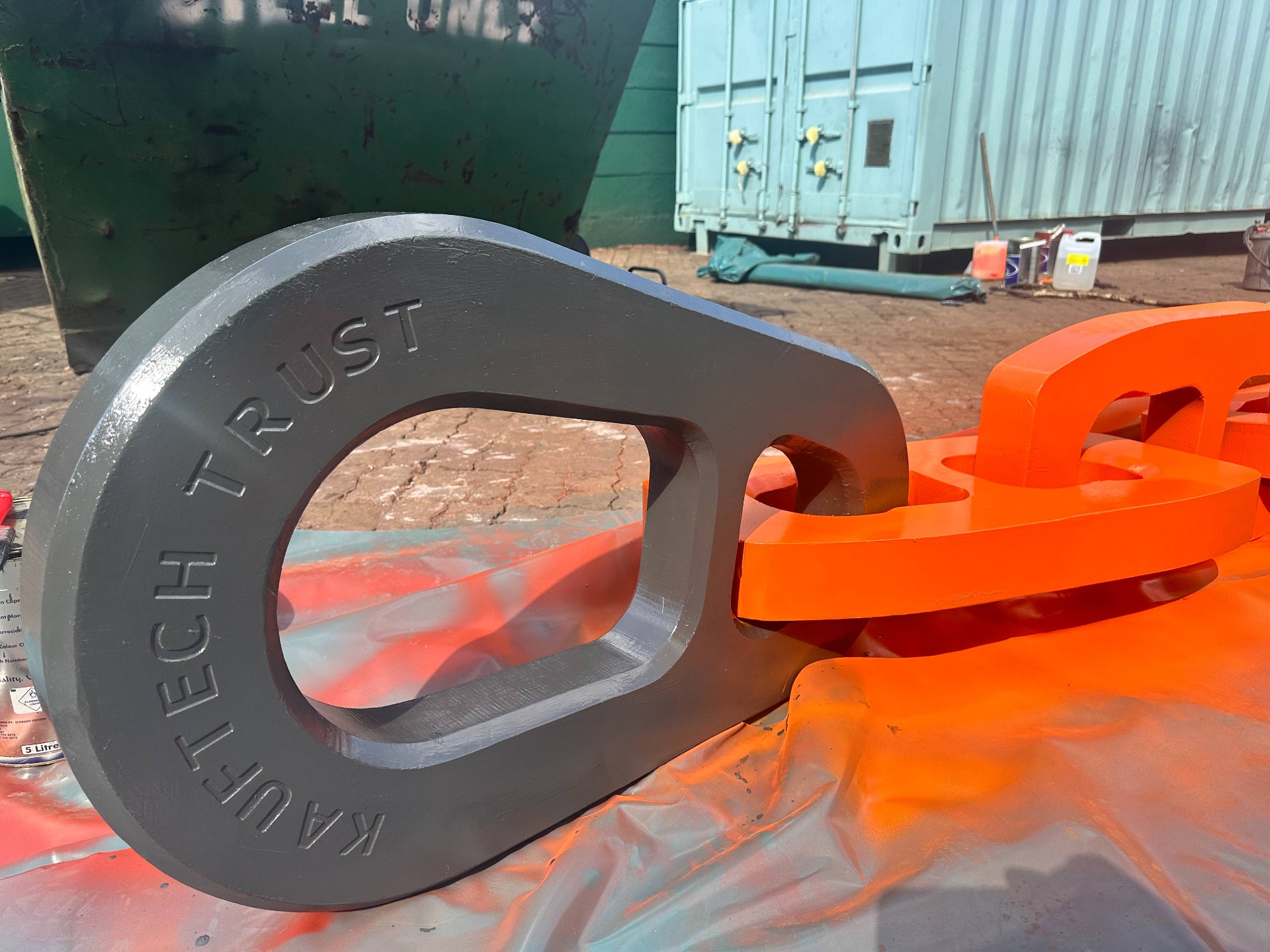 Close-up of the KAUFTECH TRUST grey end link beside an orange chain link